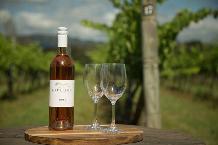 A bottle of Rosé wine is sitting on a wooden cutting board with two wine glasses.