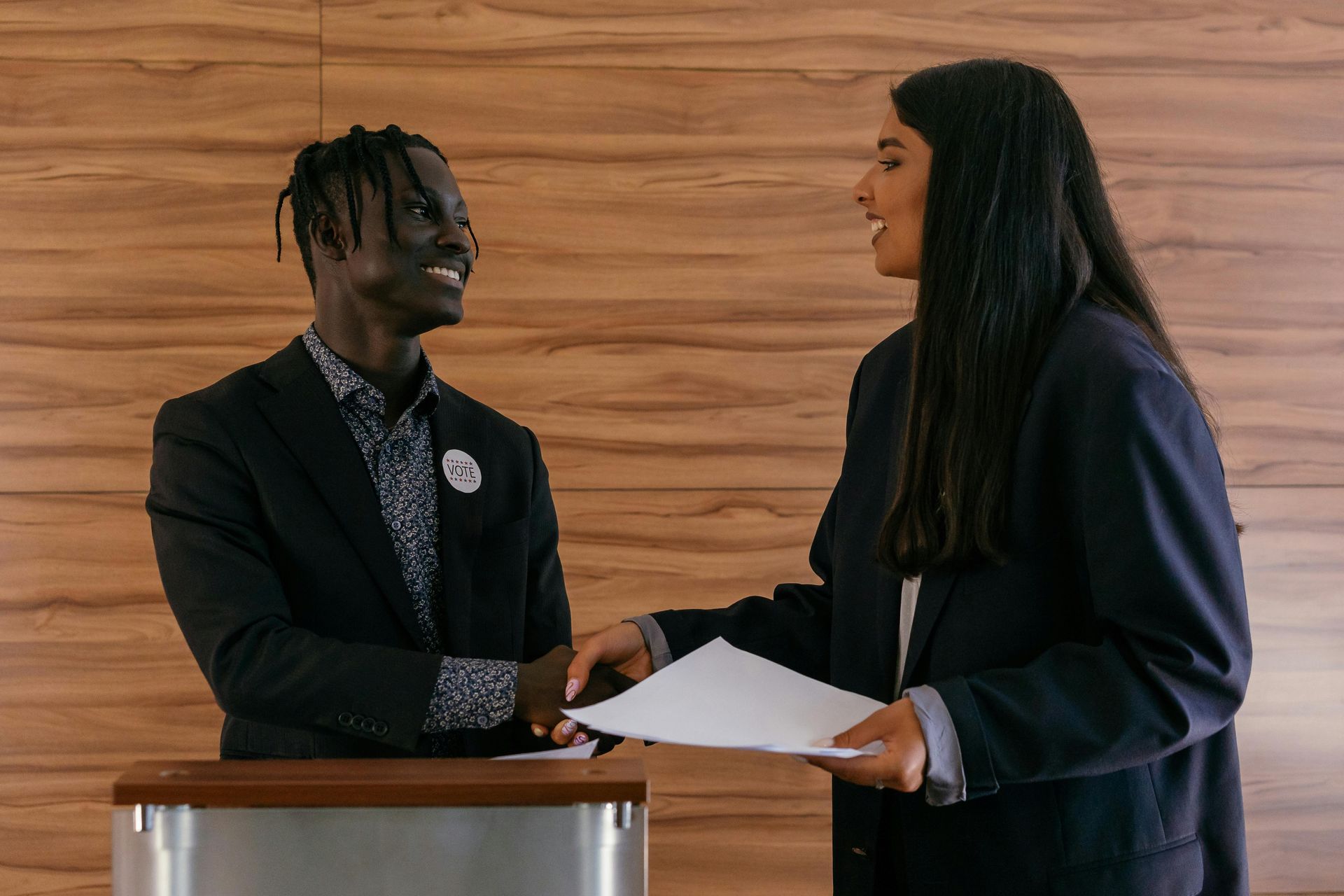 Um homem e uma mulher apertam as mãos em frente a uma parede de madeira.