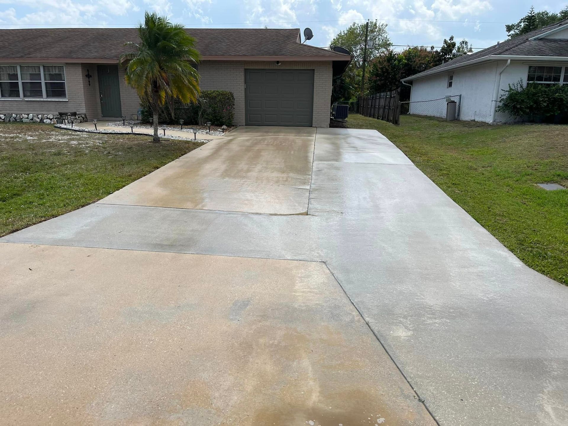 Image of a driveway in Jensen Beach, FL, residential area that has been cleaned using pressure washing. You can see a freshly cleaned driveway that is still wet. 