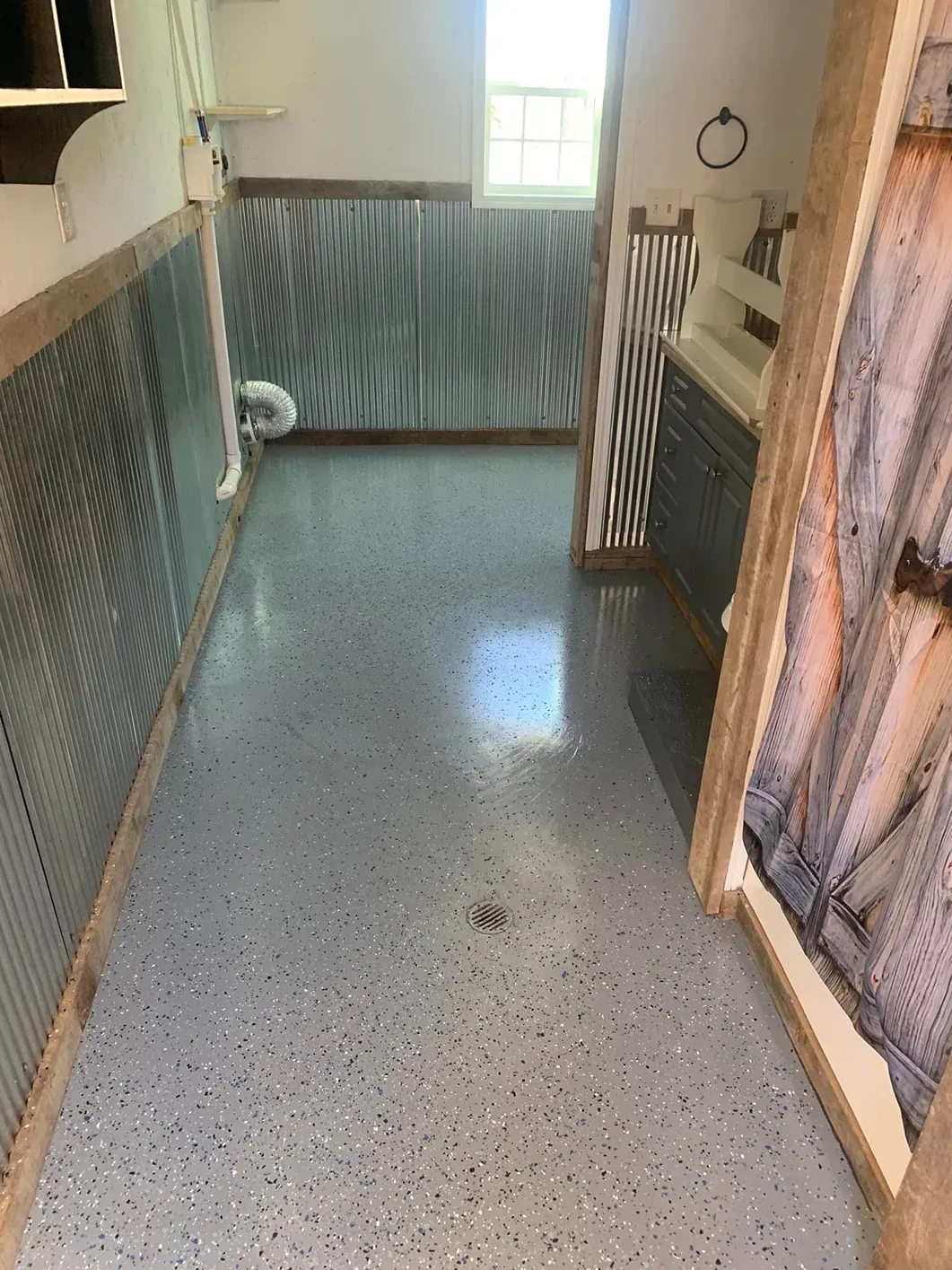 Narrow tiled room with metal railings, a window at the back, and a wet speckled floor.