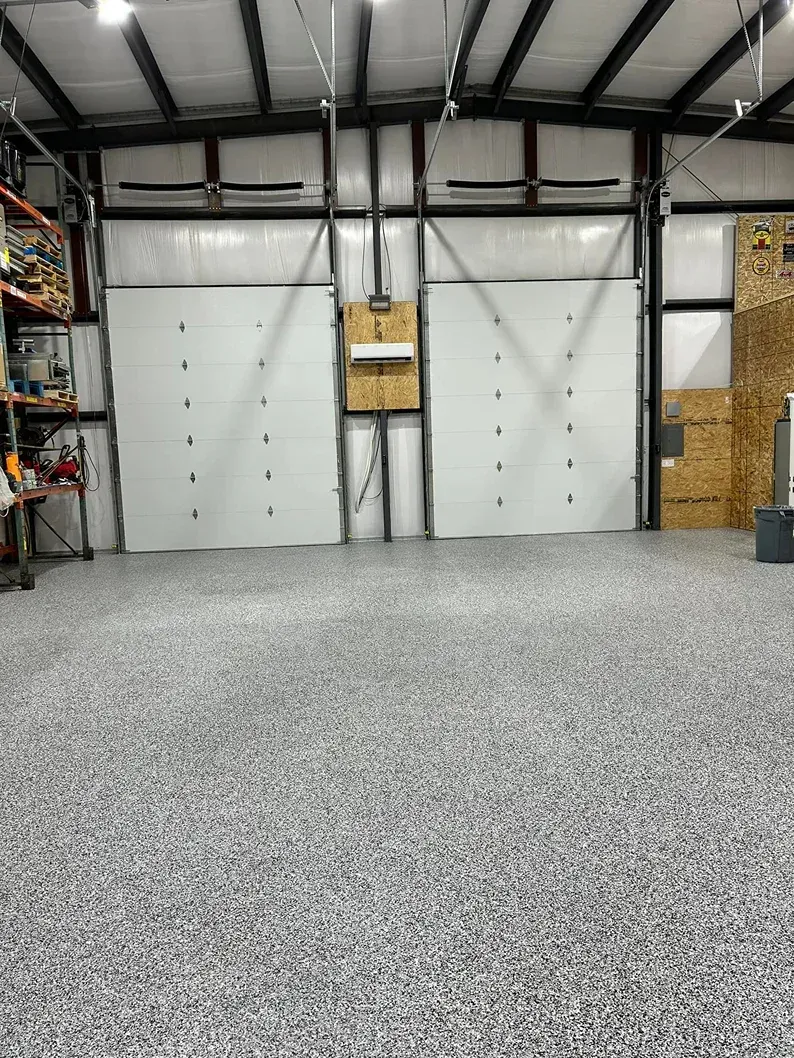 Empty industrial garage with white doors, gray concrete floor, and shelving on the sides