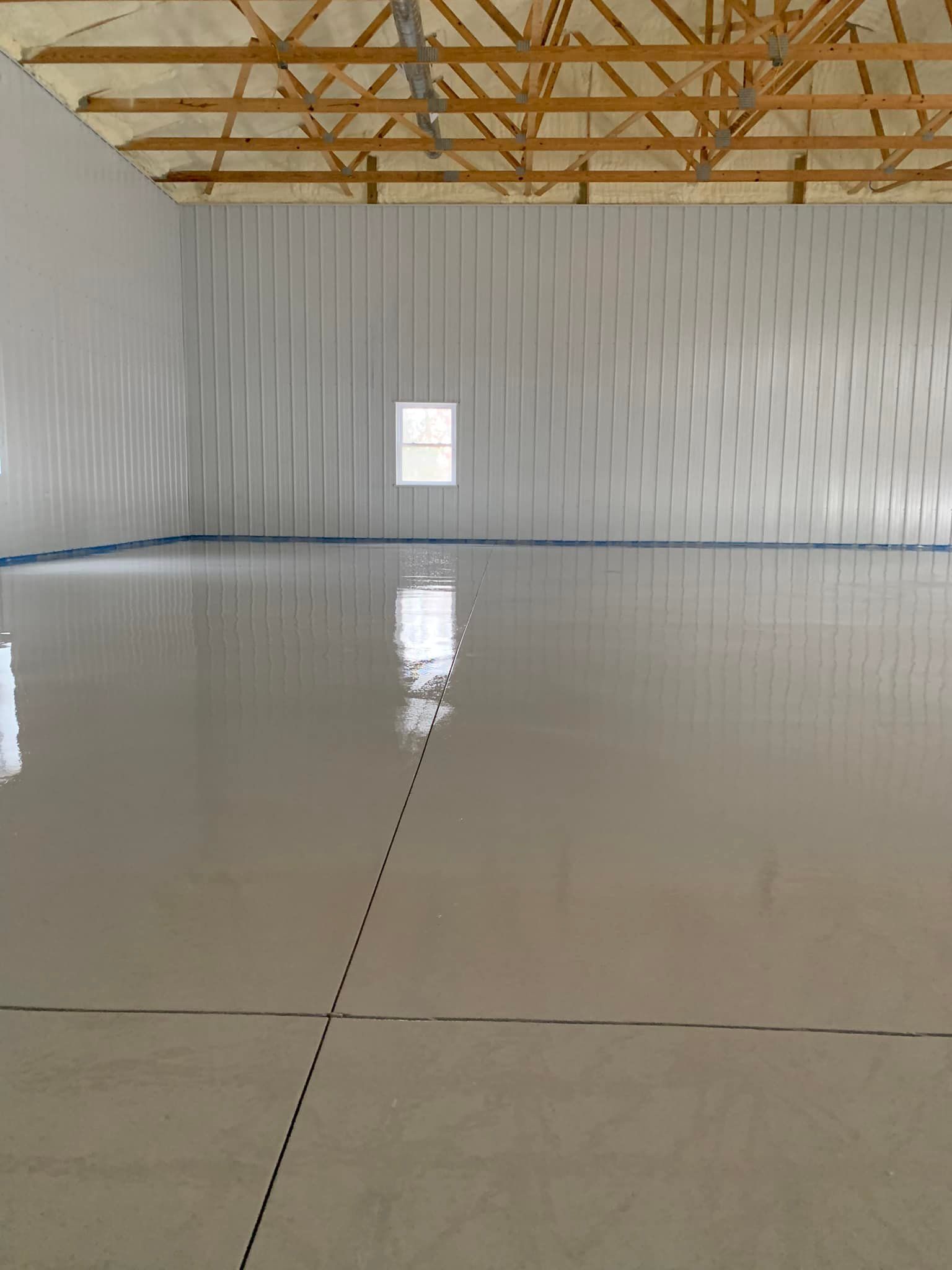 Empty warehouse interior with polished concrete floor and exposed wooden roof trusses.