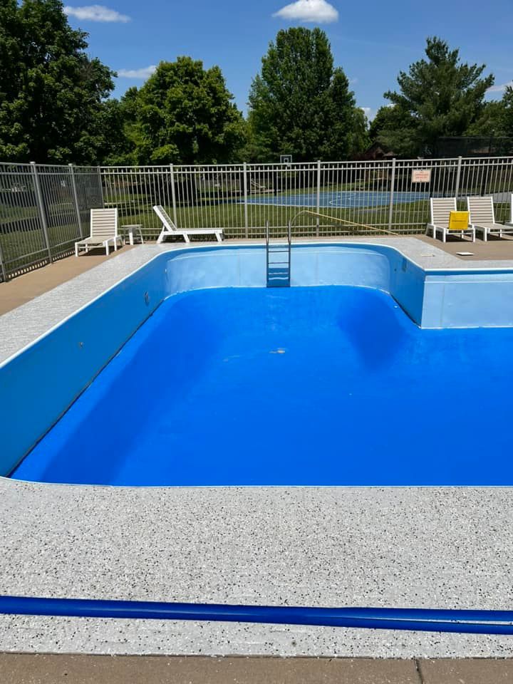 Bright blue swimming pool with a diving ladder, lounge chairs, and trees in the background