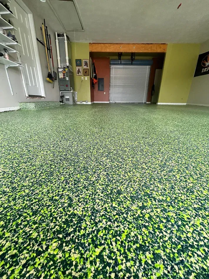 Empty indoor garage with green speckled floor and a closed metal shutter door.