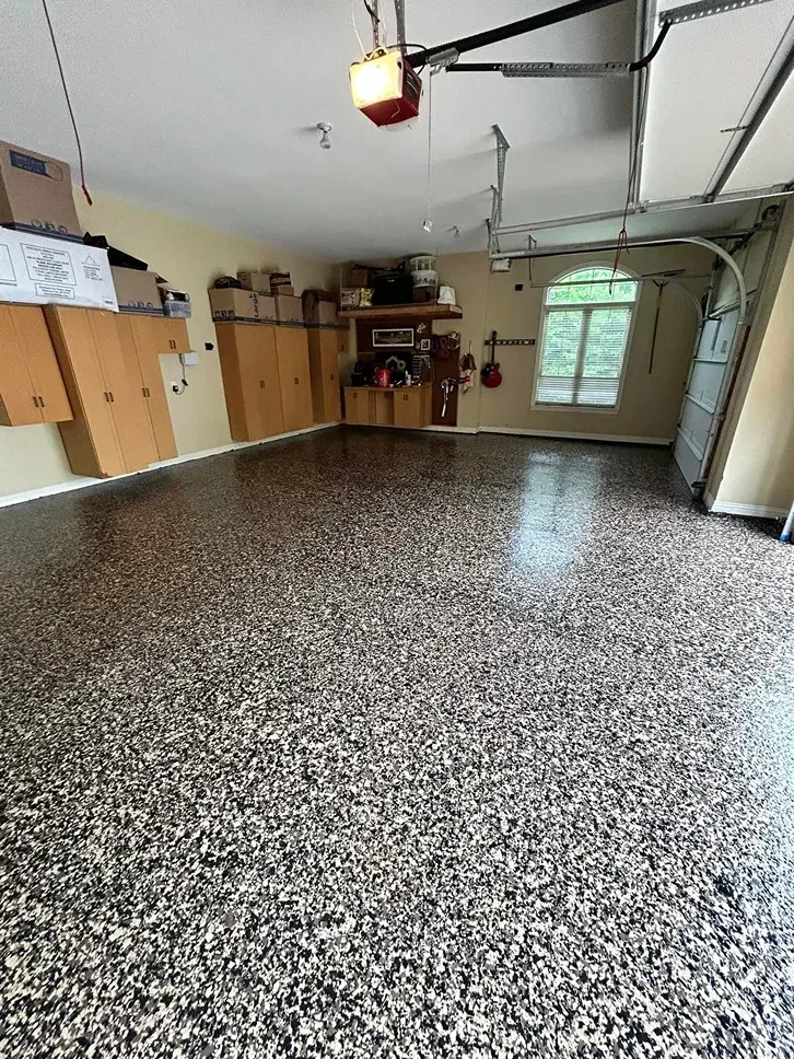 Empty garage with speckled floor, wooden cabinets, open door, and a windowed entryway.