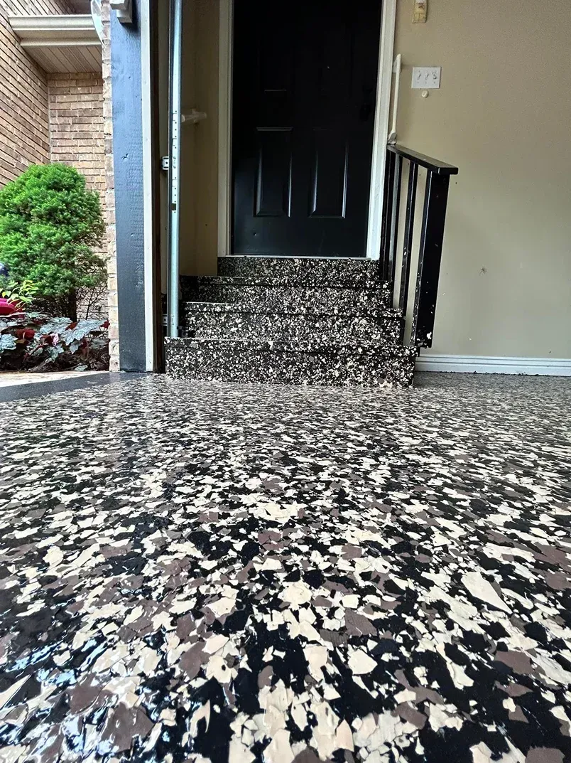 Black-and-white speckled entry floor leading to a dark front door with steps and a railing