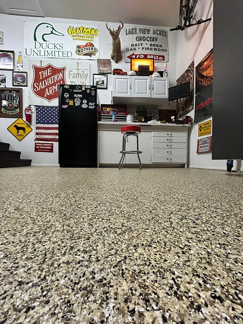 Garage-style room with a black mini fridge, white cabinets, a stool, and many wall signs and posters.