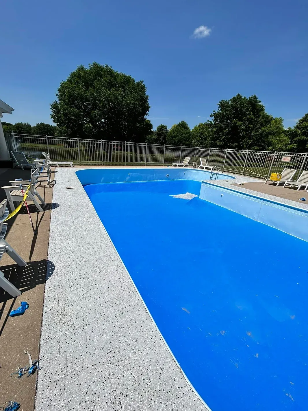 Outdoor swimming pool with bright blue water, white deck, and lounge chairs under a clear sky