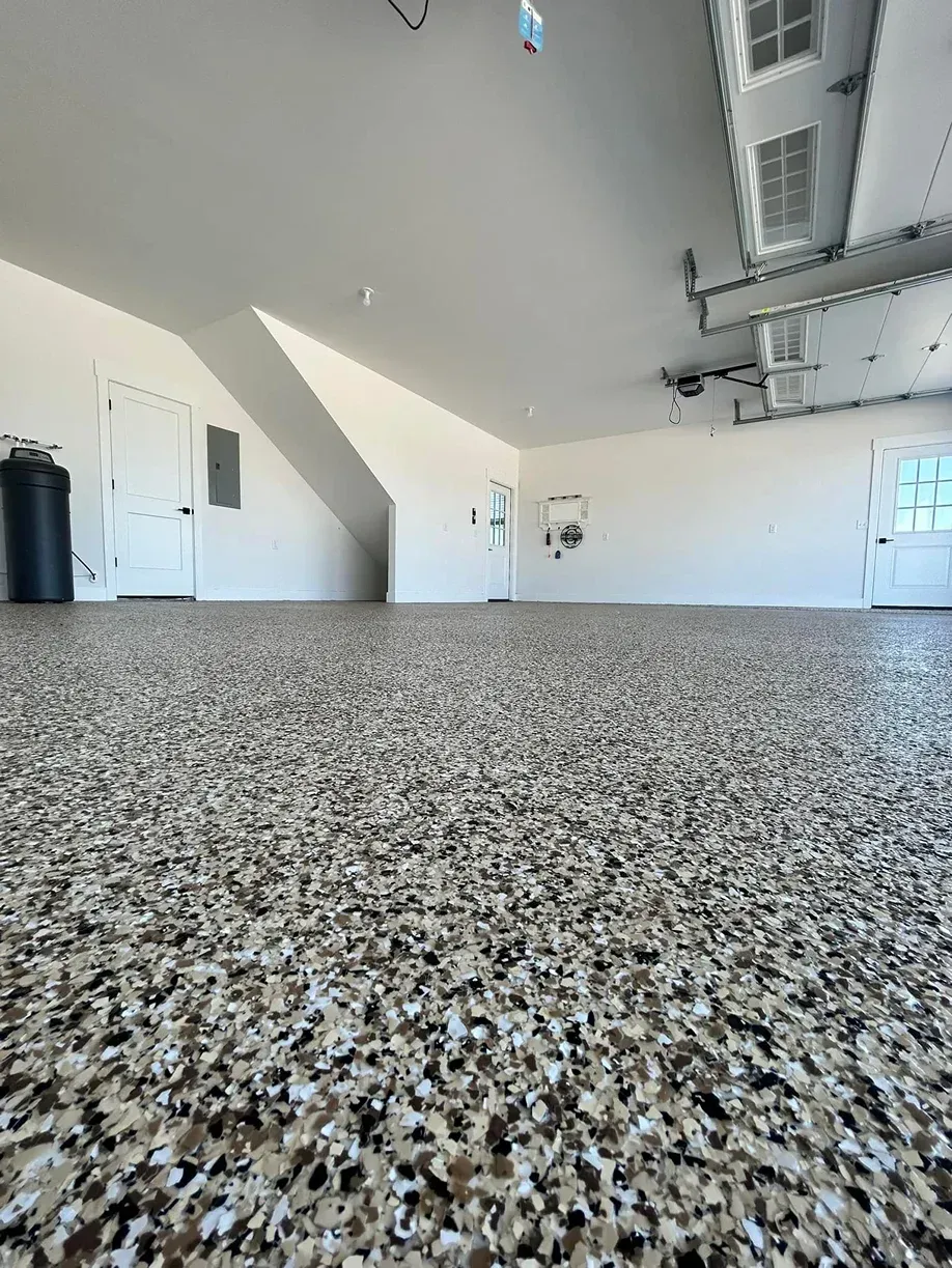 Empty garage with speckled epoxy floor, white walls, and overhead door tracks.