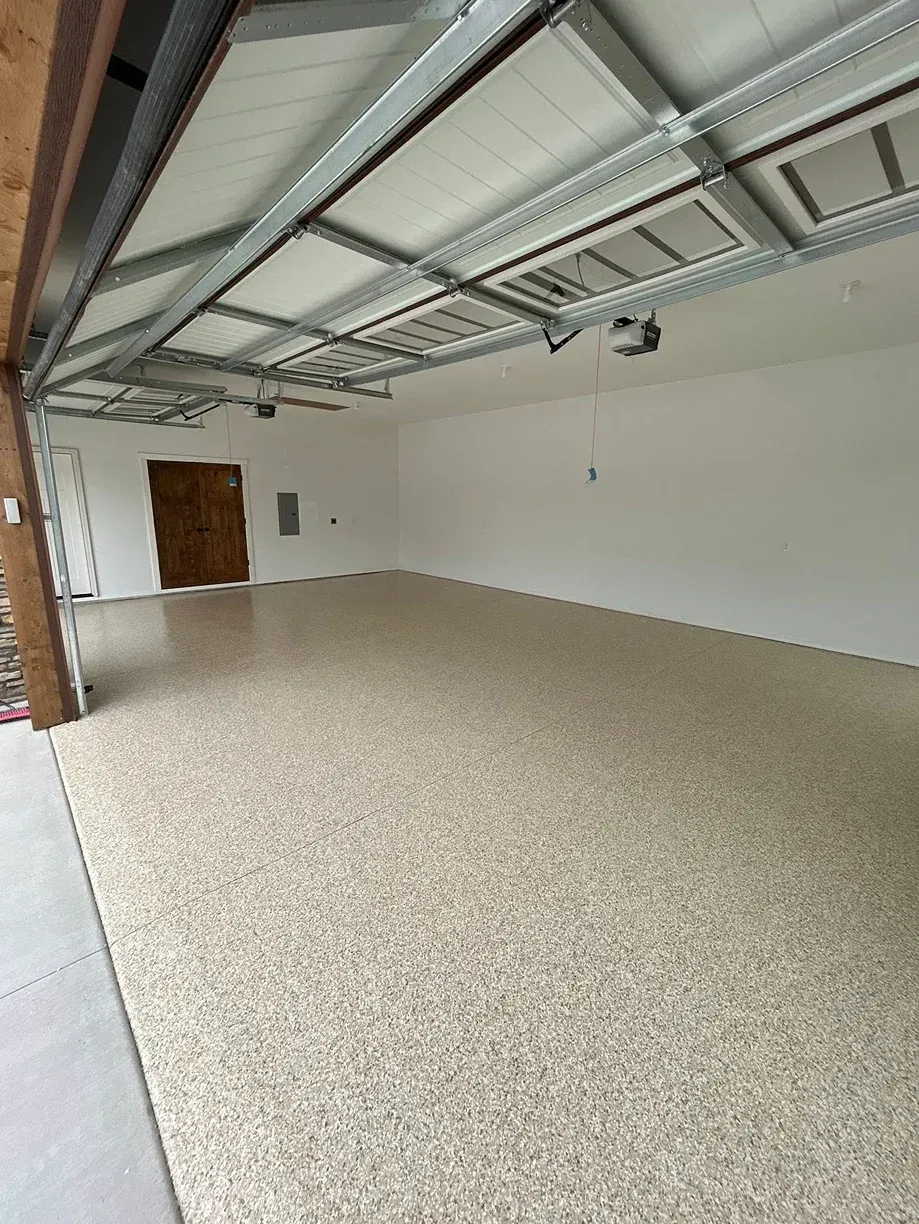 Empty garage interior with beige floor, white walls, and exposed ceiling beams