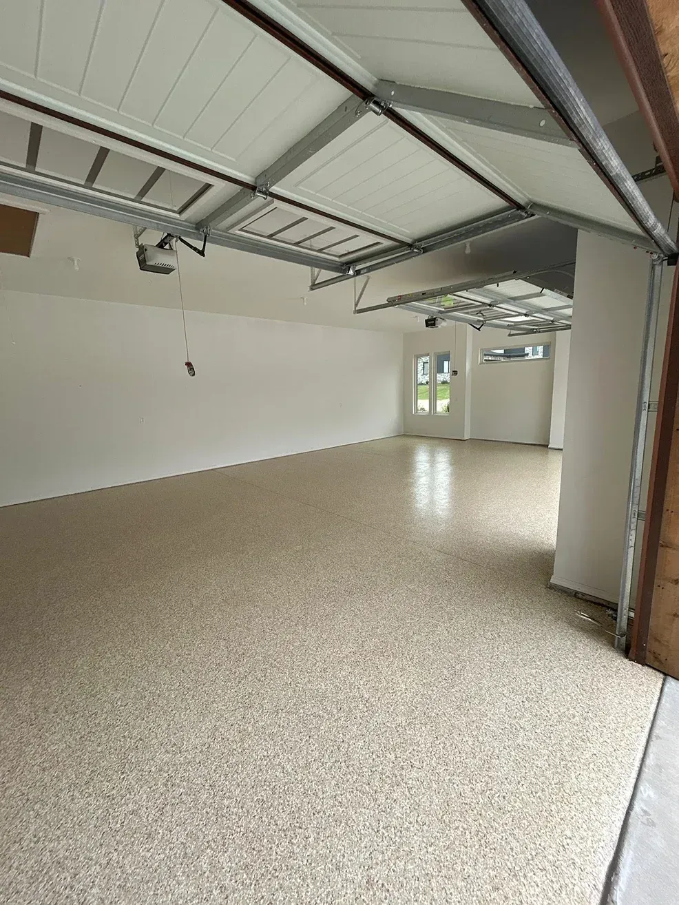 Empty garage interior with beige speckled floor, white walls, and an open ceiling with exposed beams