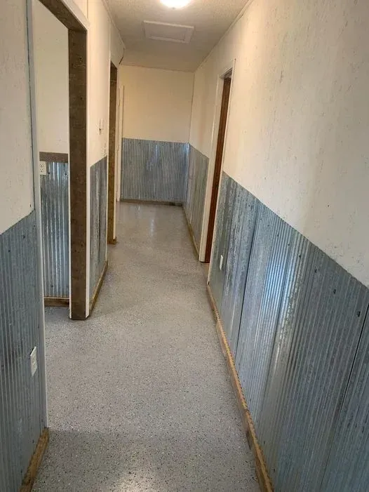 Narrow hallway with beige walls, corrugated metal wainscoting, and a gray floor.