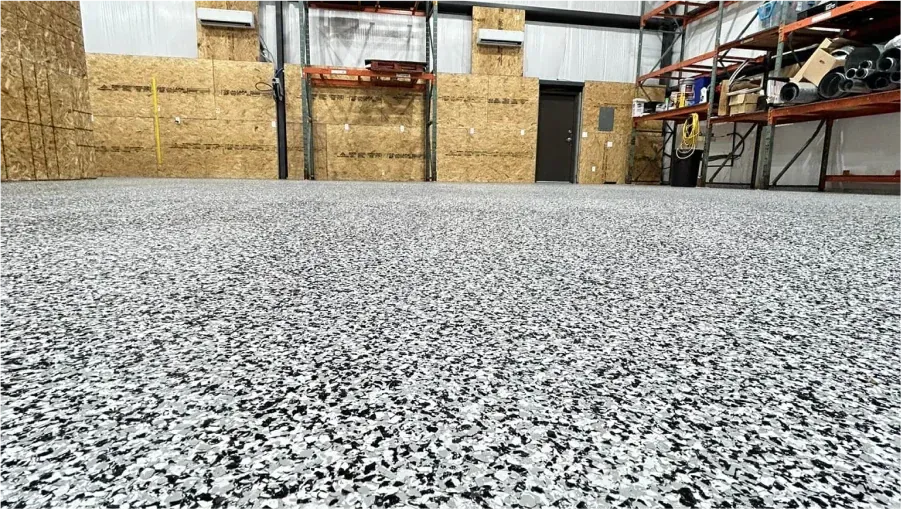 Industrial warehouse interior with speckled epoxy floor, plywood walls, and metal storage racks.