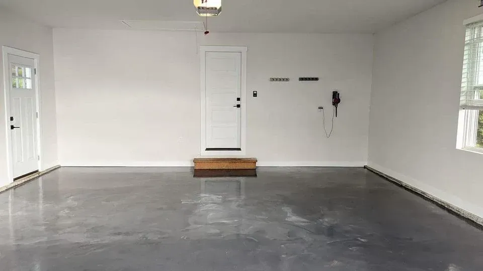 Empty garage with gray floor, white walls, a centered door, and windows on both sides.