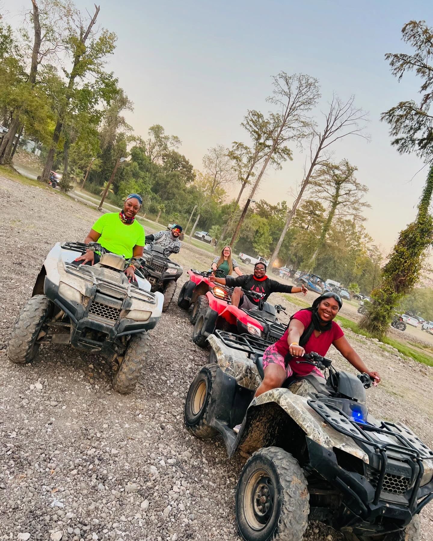 A group of people riding ATVs on a gravel trail surrounded by trees on a sunny day.