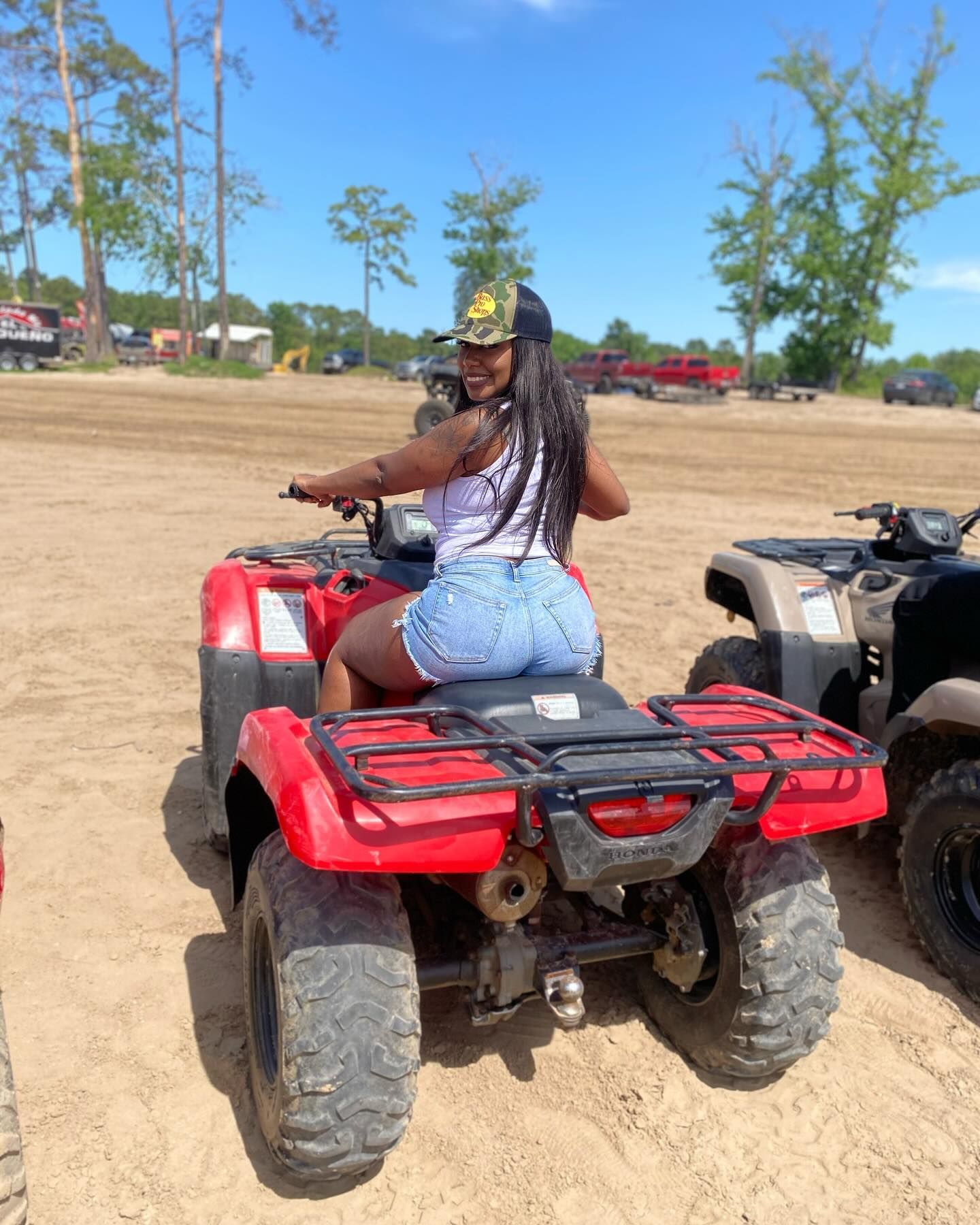 A person smiling while sitting on a red ATV on a sandy, open field under a clear blue sky.