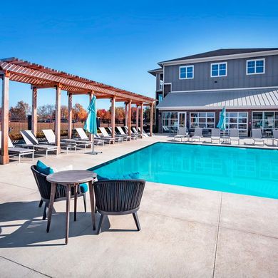 A large swimming pool with chairs and tables in front of a building at Flats at Stones Crossing.