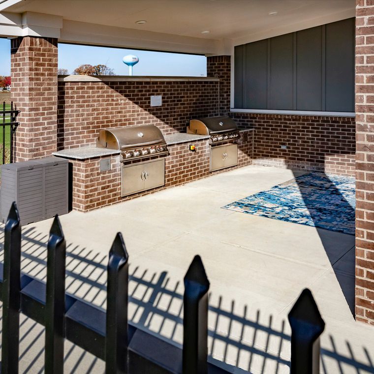 A brick building with a grill and a fence in front of it at Flats at Stones Crossing.