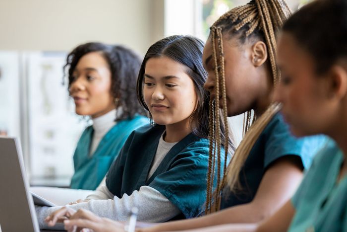 a group of nurses are sitting at a table using laptops .