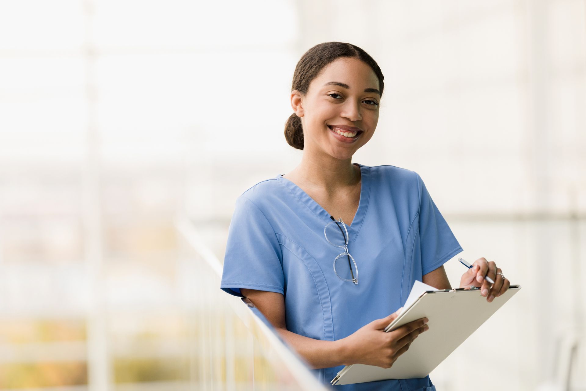 a nurse is smiling while holding a clipboard and a pen .