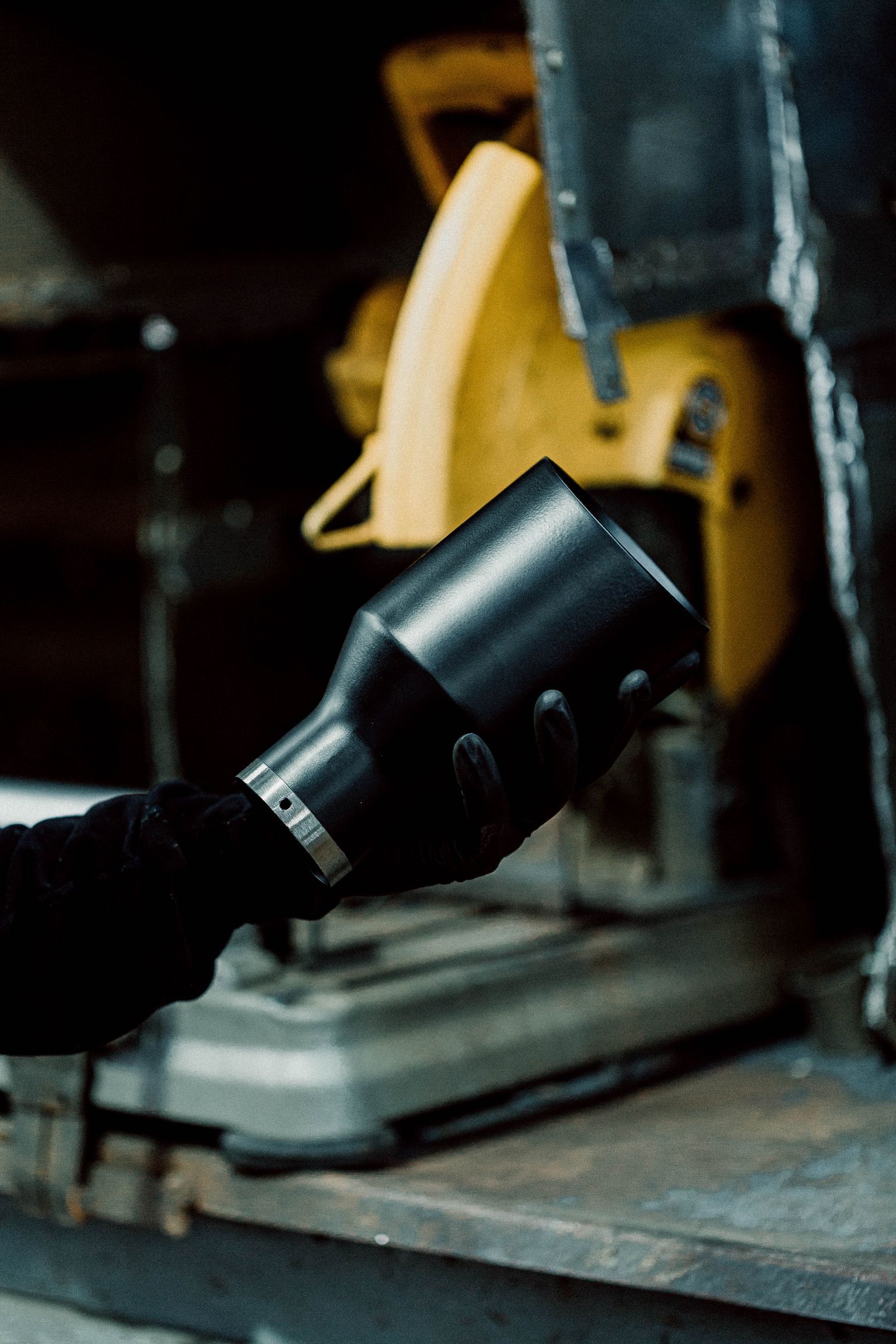 A person is holding a vacuum cleaner in front of a circular saw.