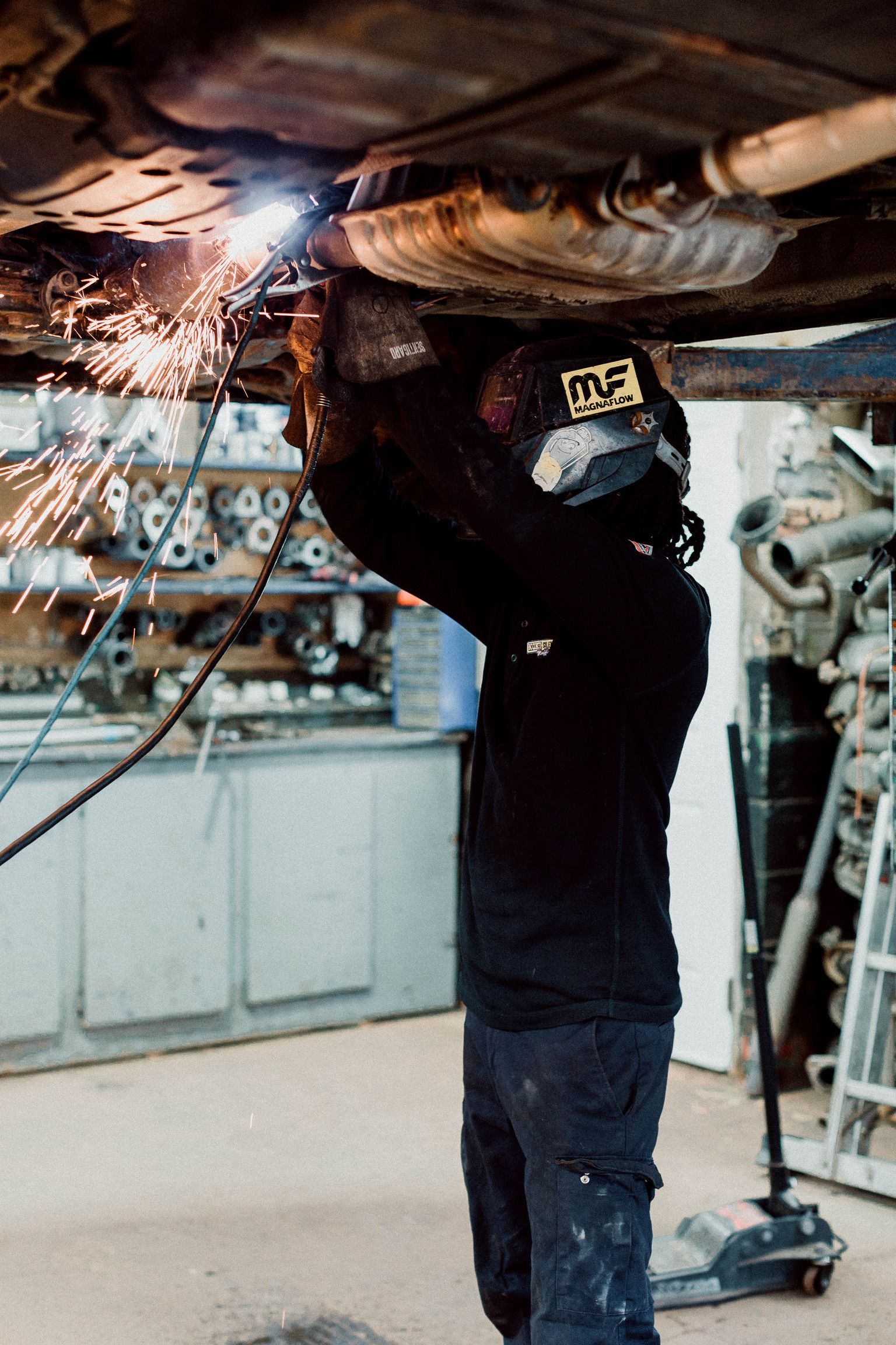 A man is welding under a car in a garage.