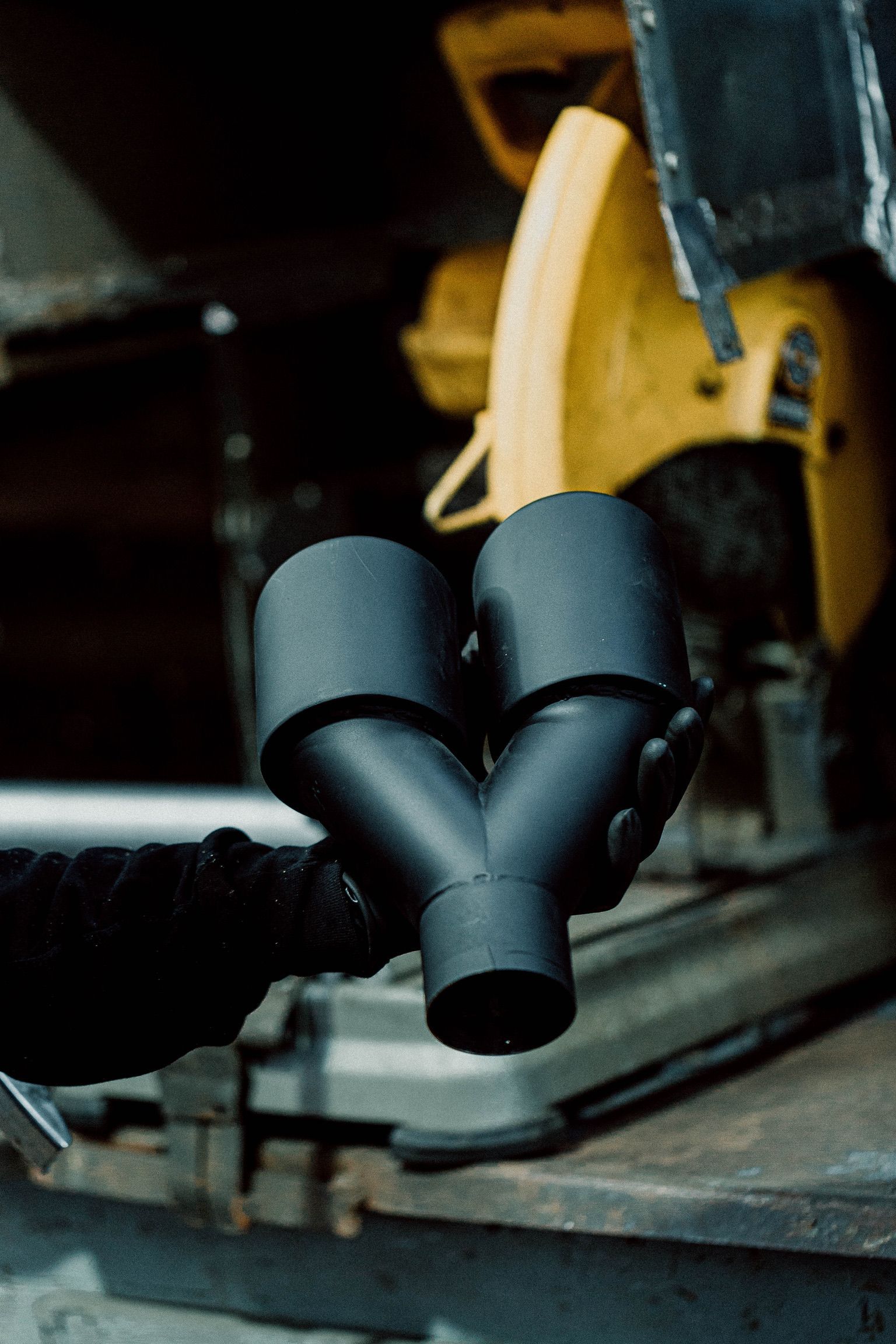 A person is holding a black pipe with a yellow saw in the background.