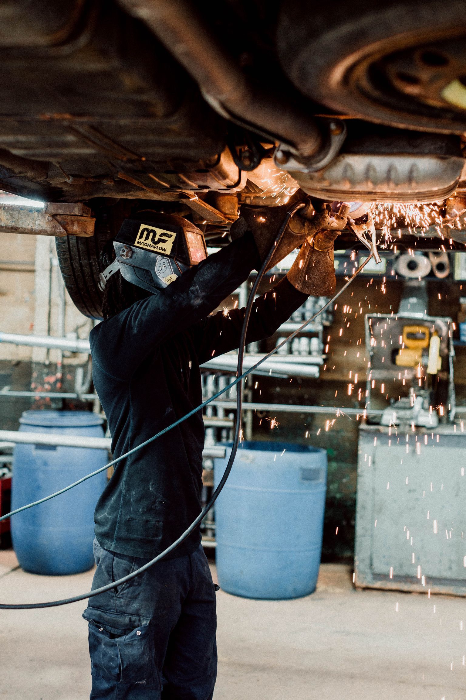 A man is welding under a car in a garage.