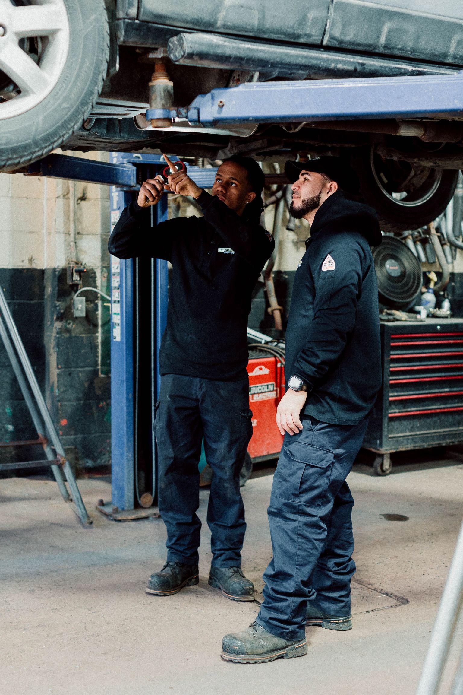 Two men are working on a car on a lift in a garage.