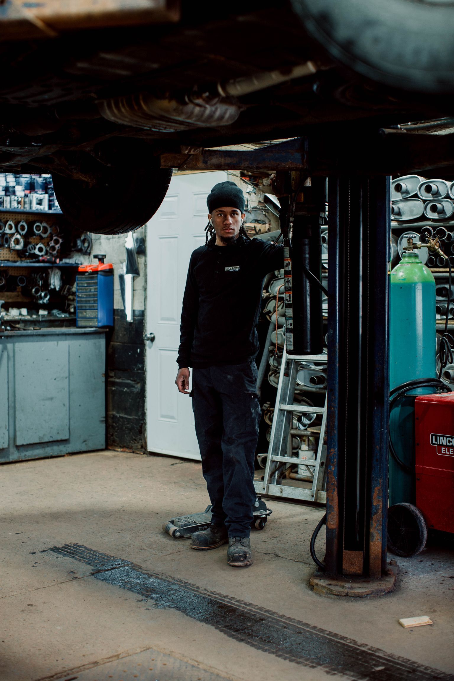 A man is standing under a car on a lift in a garage.