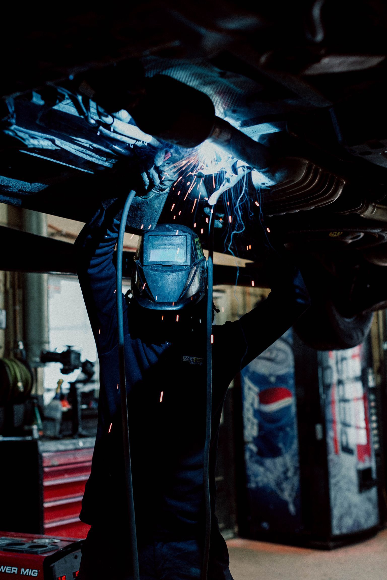 A man is welding under a car in a garage.