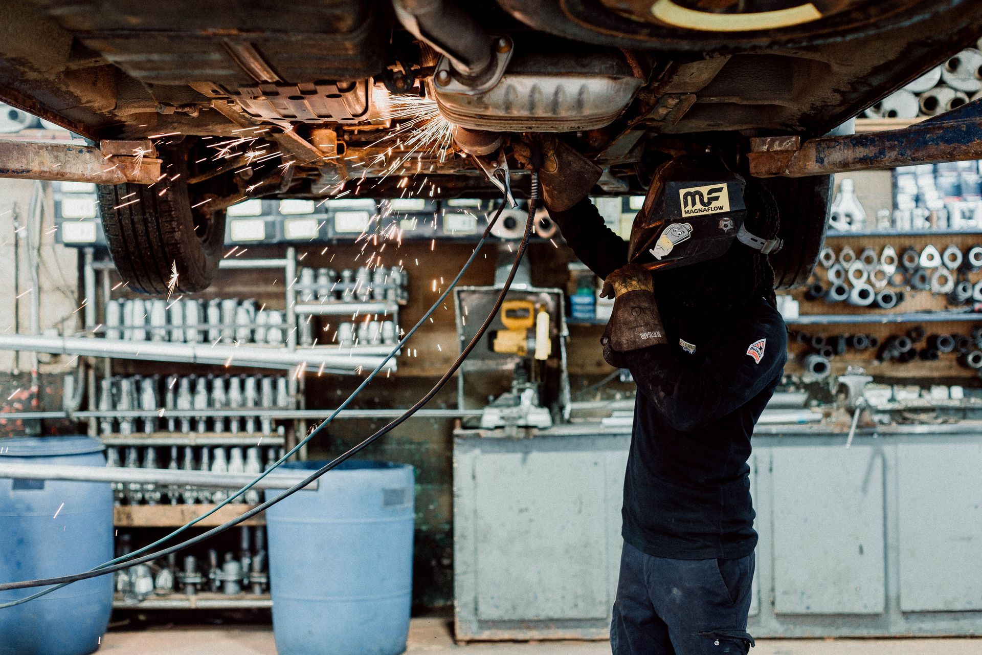 A man is welding under a car in a garage.