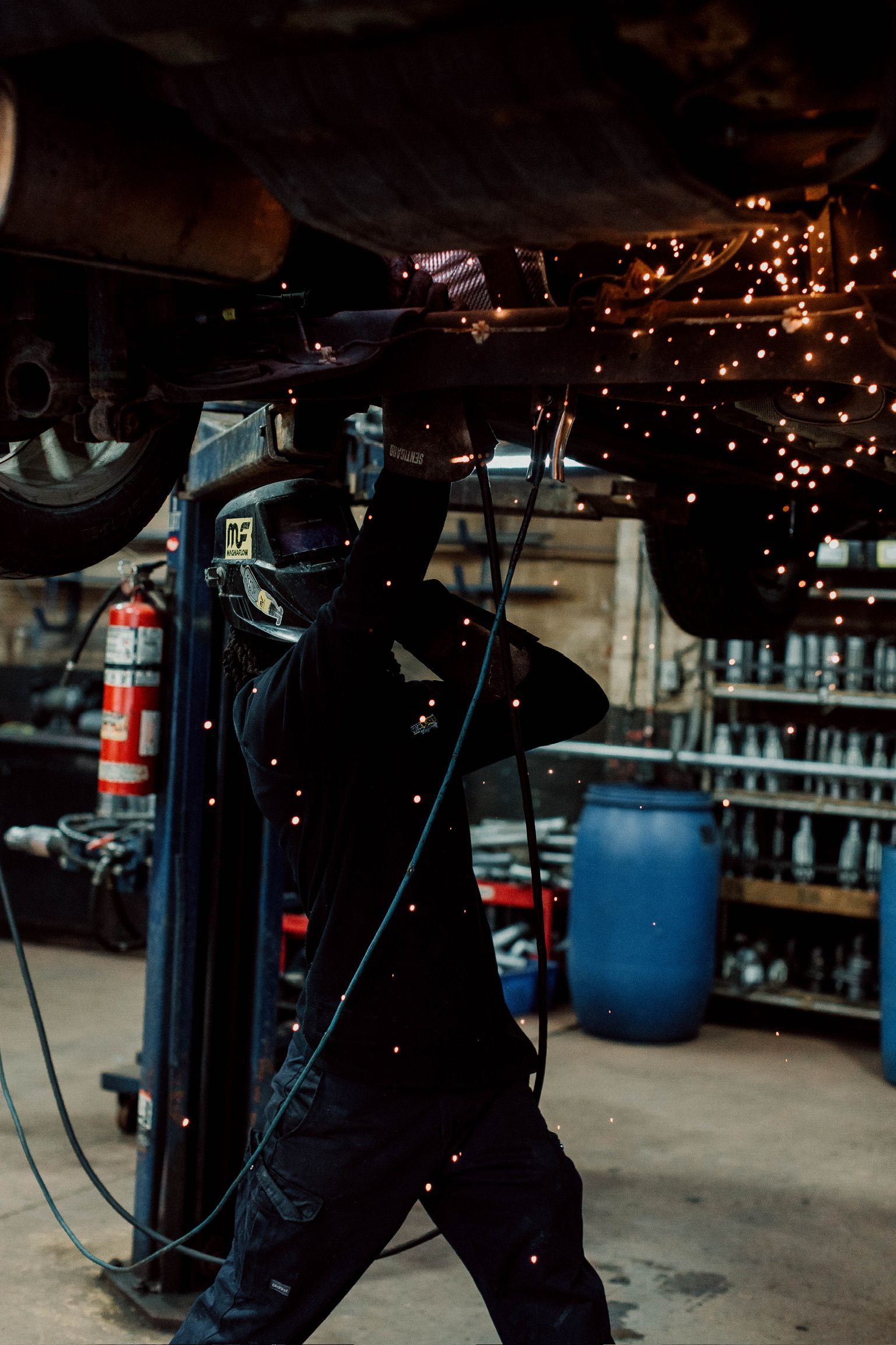 A man is welding under a car in a garage.