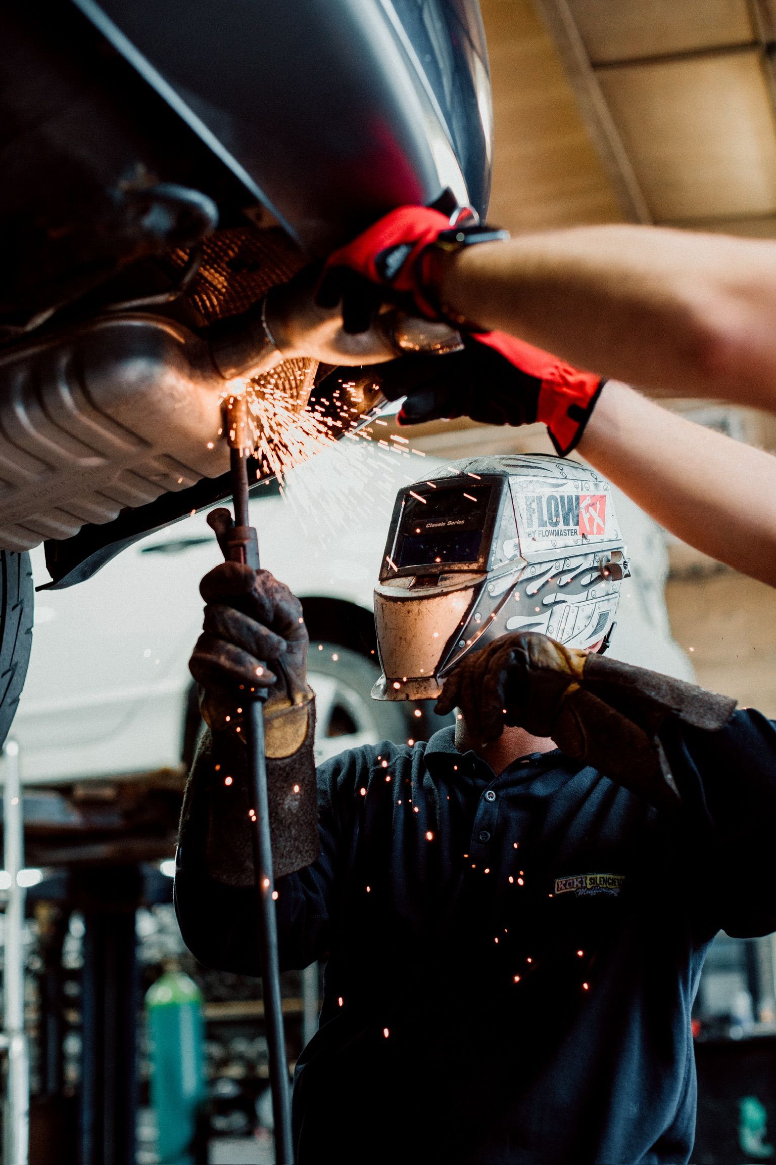 A man is welding the exhaust pipe of a car in a garage.