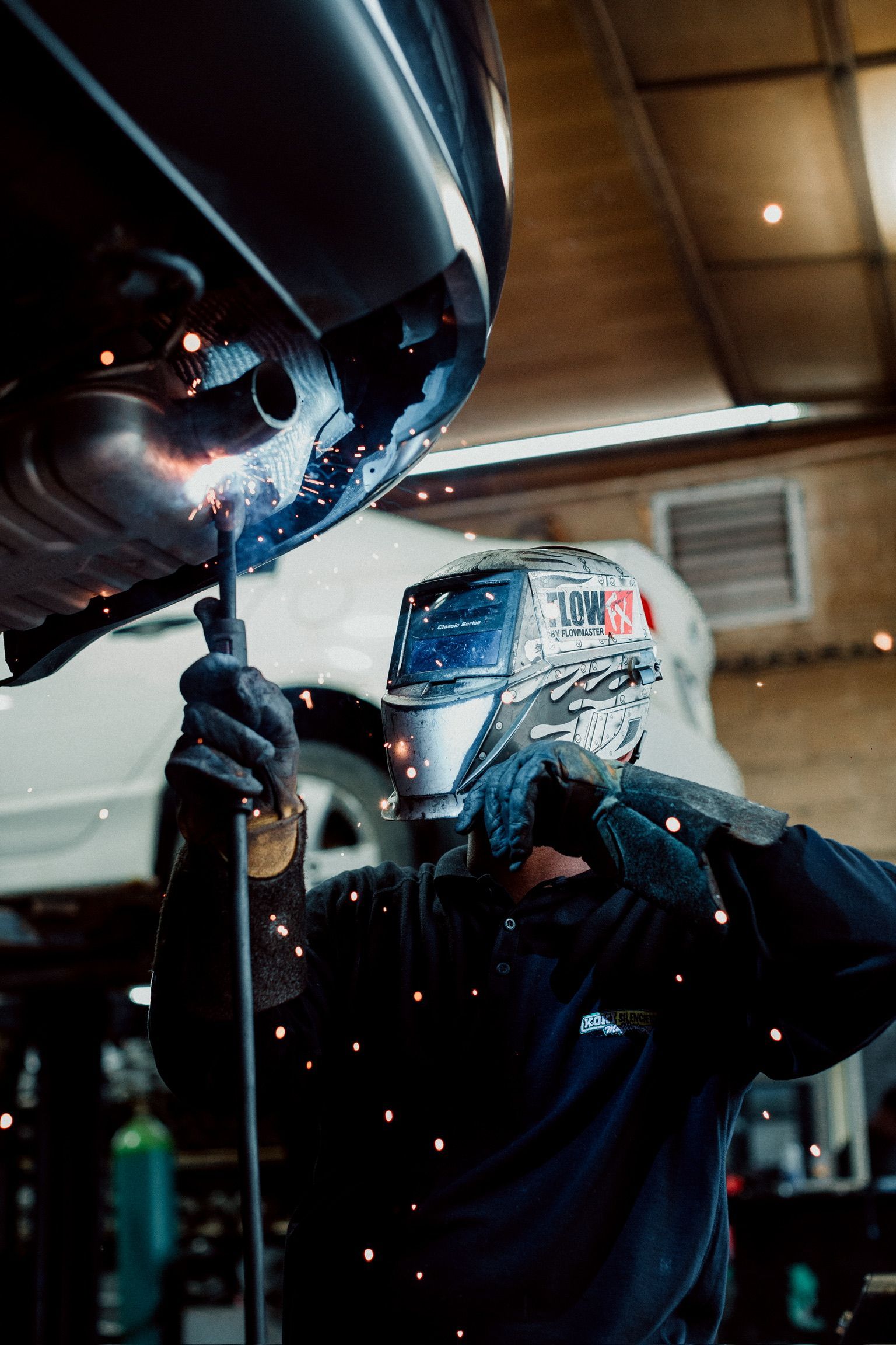 A man is welding a car exhaust pipe in a garage.