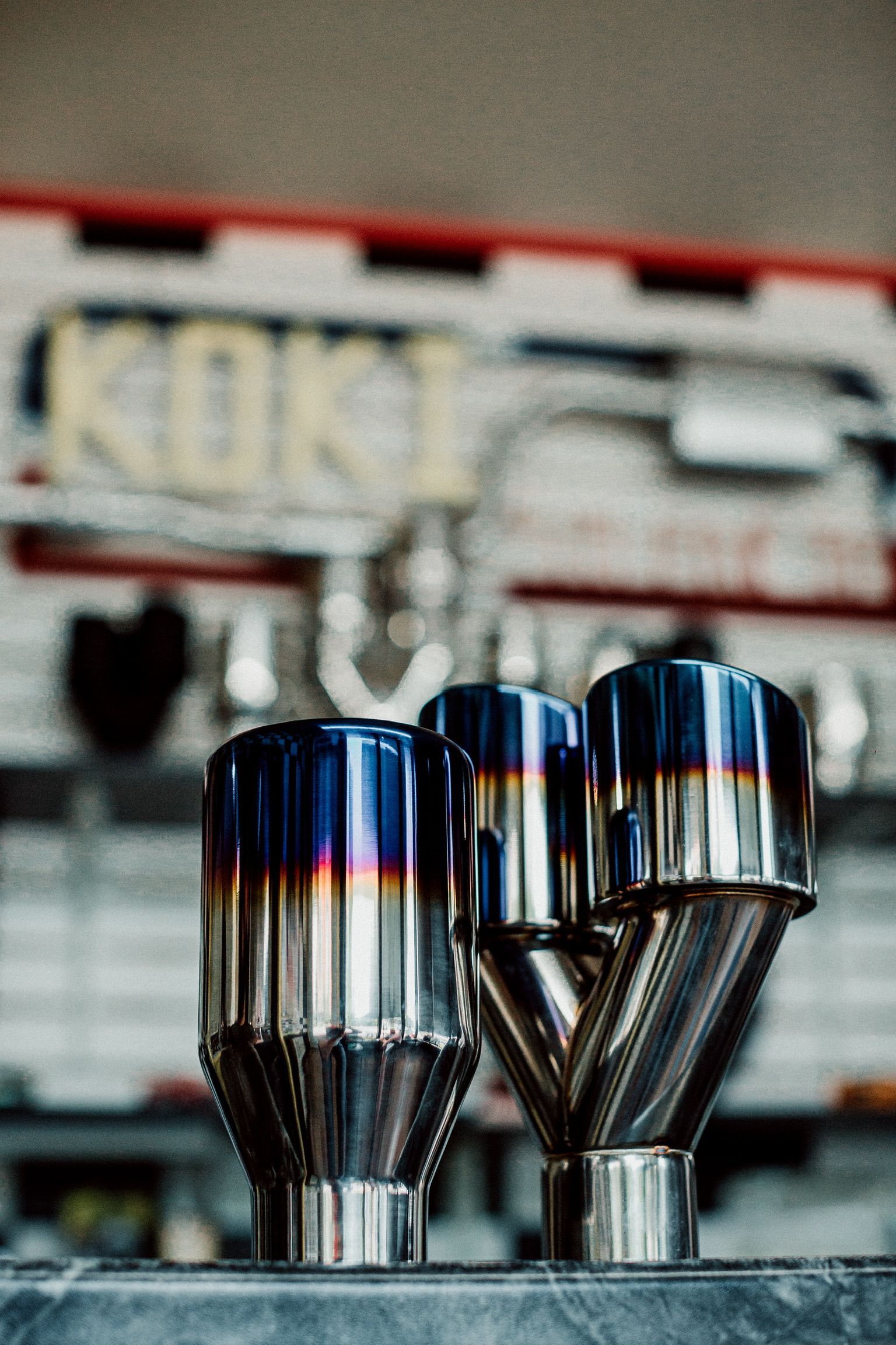 Two exhaust pipes are sitting on a table in front of a sign that says koki