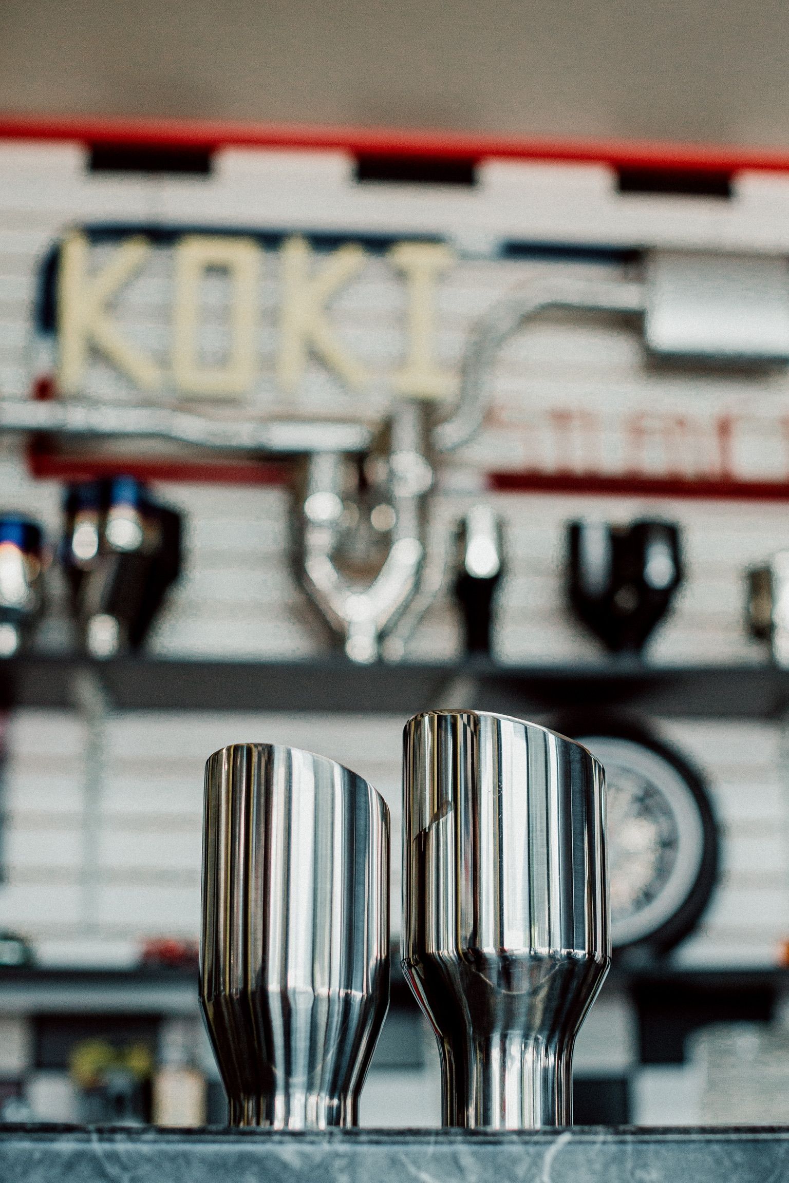 Two stainless steel cups are sitting on a counter in front of a sign that says koki.