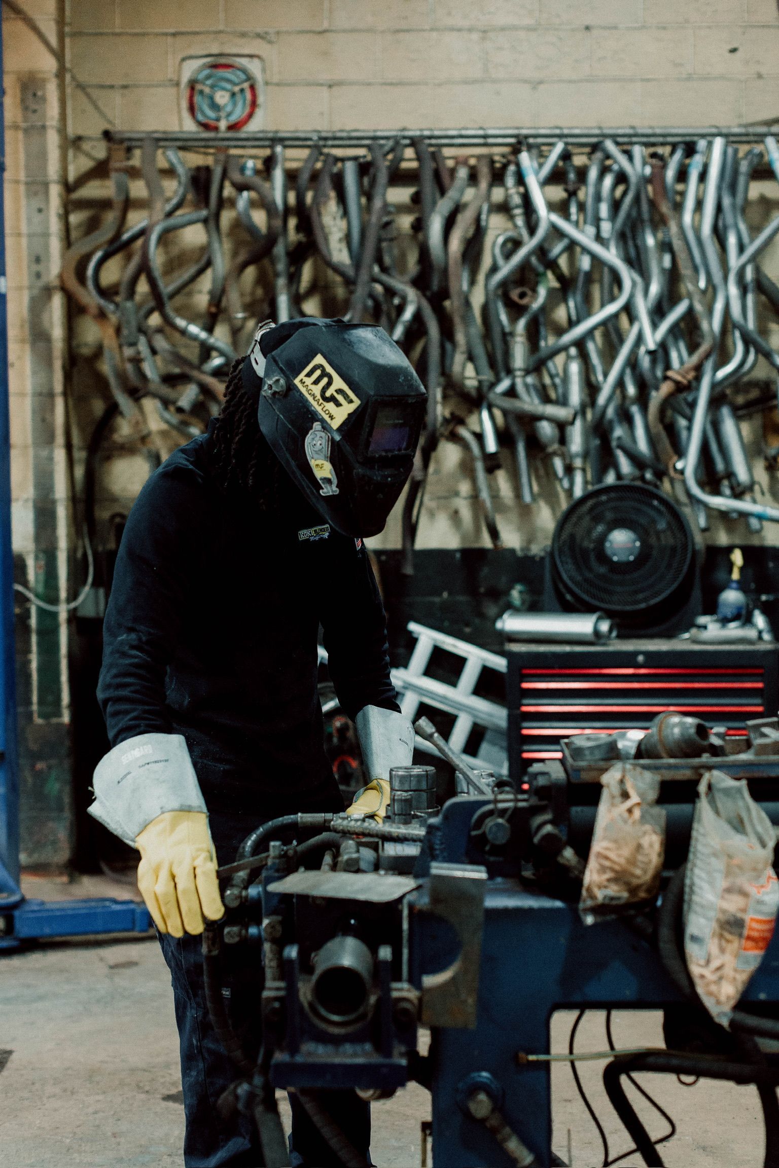 A man wearing a welding helmet is working on a machine in a garage.