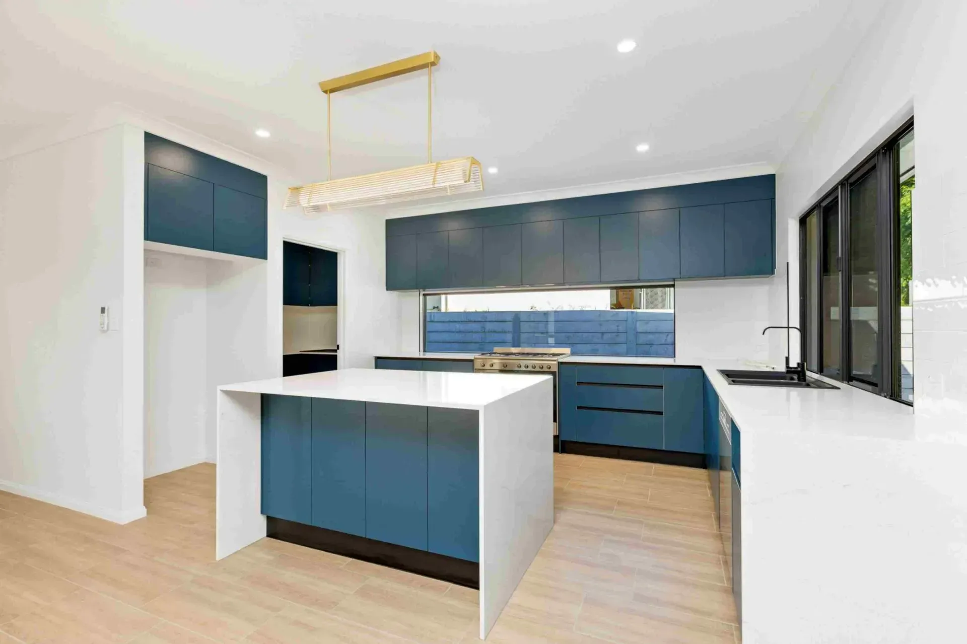 A Kitchen With Blue Cabinets, White Counter Tops, and a Large Island — Ashlee Jones Homes in Mission Beach, QLD