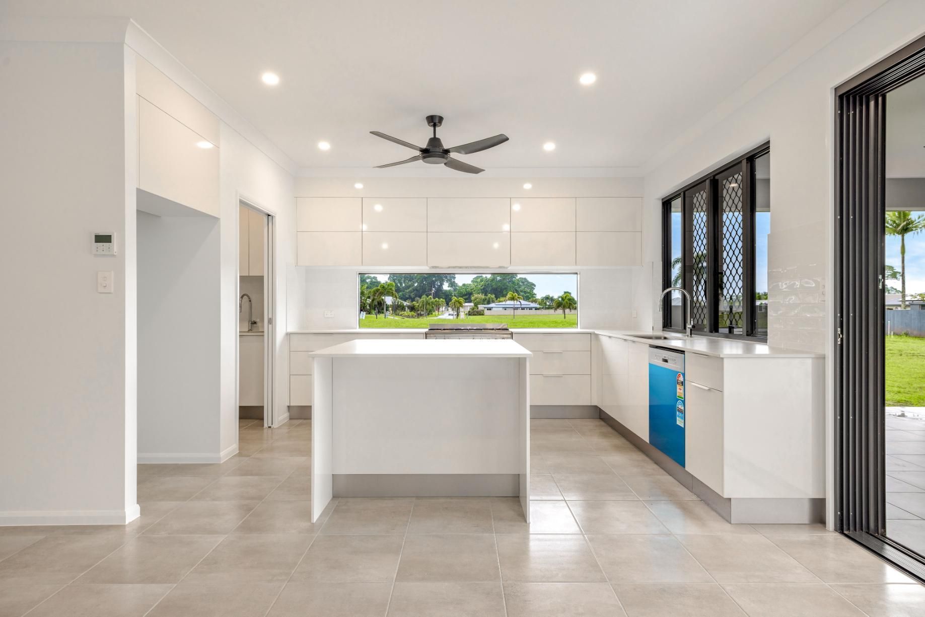 An Empty Kitchen With White Cabinets and a Ceiling Fan — Ashlee Jones Homes in Gordonvale, QLD