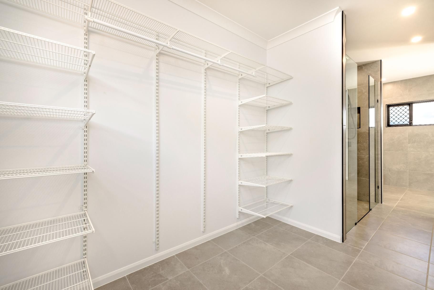 An Empty Walk in Closet With White Shelves and a Walk in Shower — Ashlee Jones Homes in Gordonvale, QLD