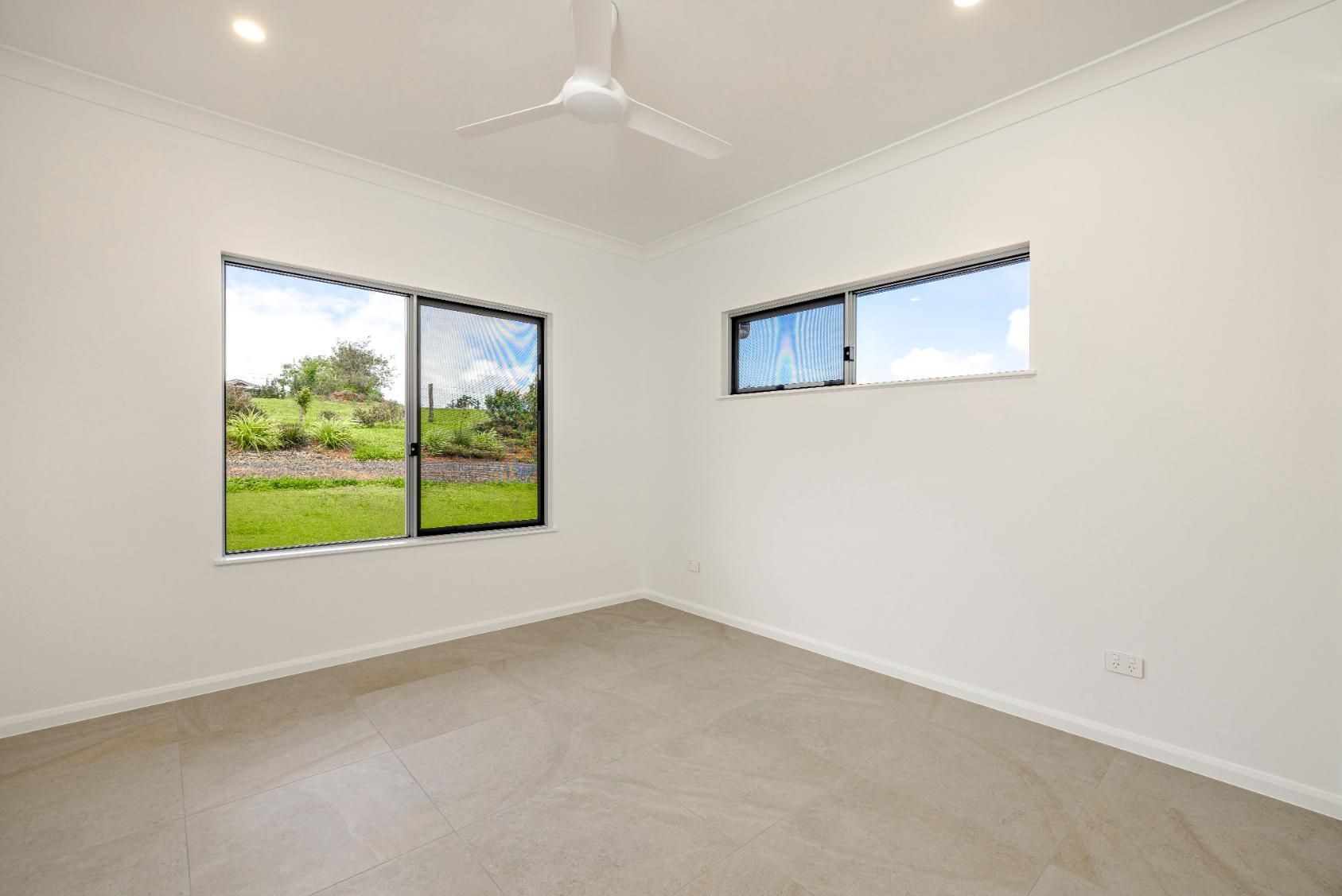 An empty bedroom with two windows and a ceiling fan.
