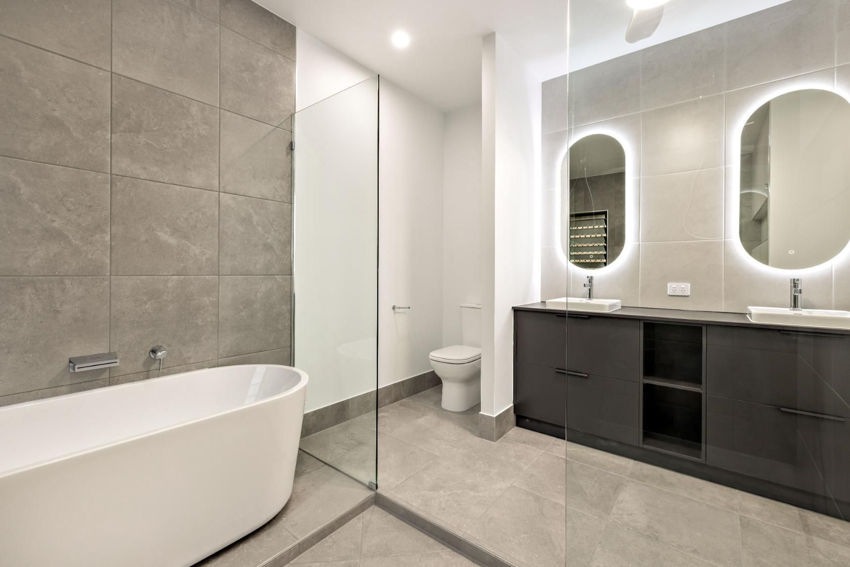 A Bathroom With a Bathtub, Toilet, Sink and Mirrors — Ashlee Jones Homes in Gordonvale, QLD