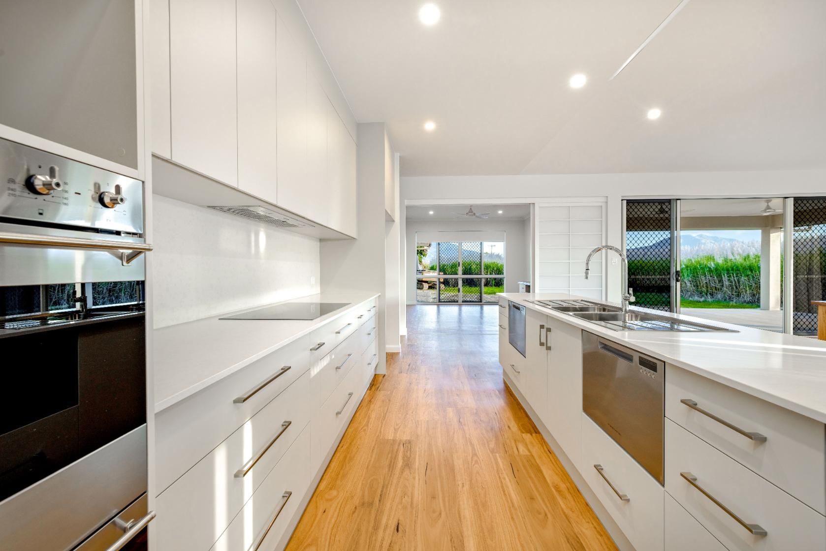 A Kitchen With White Cabinets , Stainless Steel Appliances , and Hardwood Floors — Ashlee Jones Homes in Gordonvale, QLD