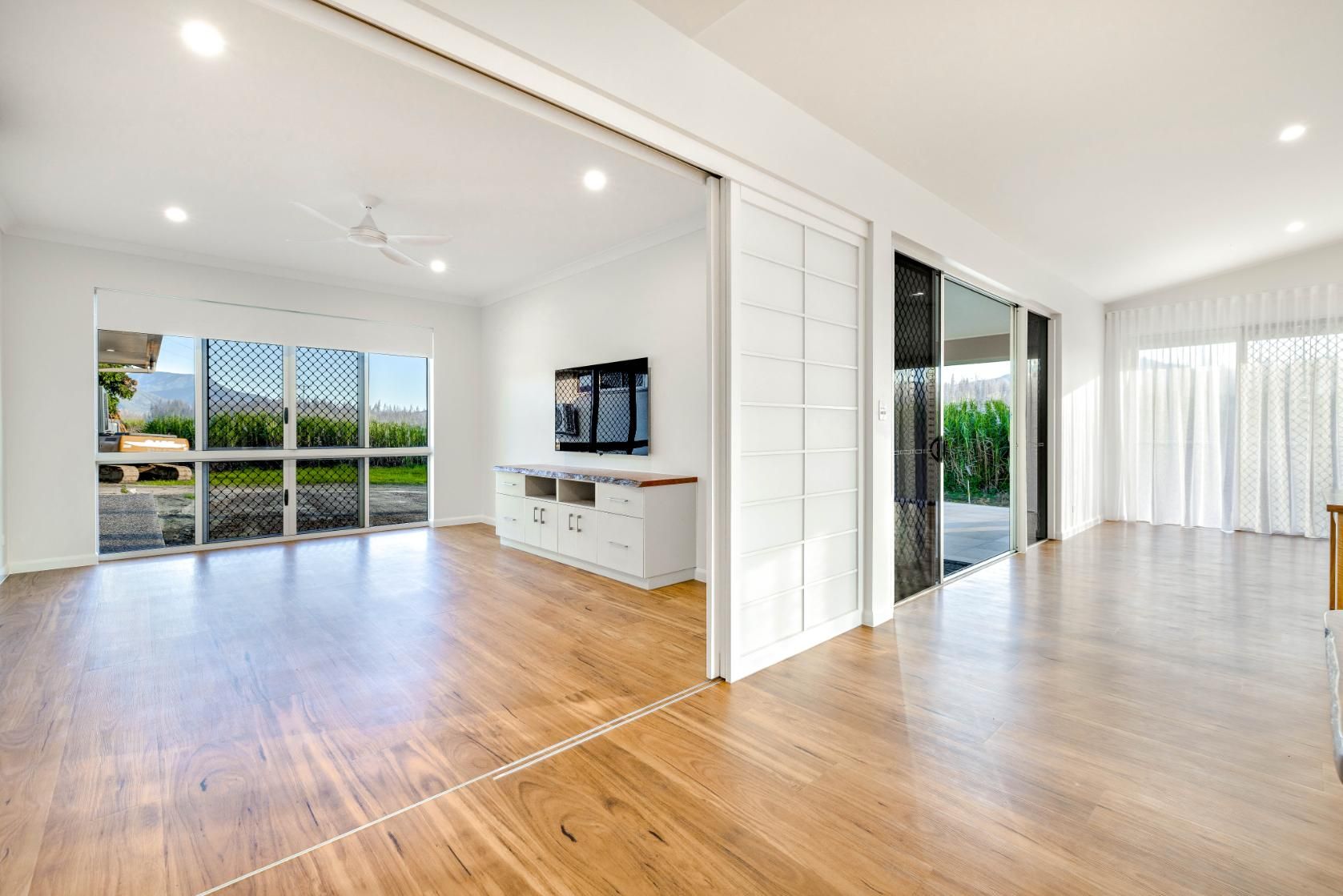 An Empty Living Room With Hardwood Floors and Sliding Glass Doors — Ashlee Jones Homes in Gordonvale, QLD
