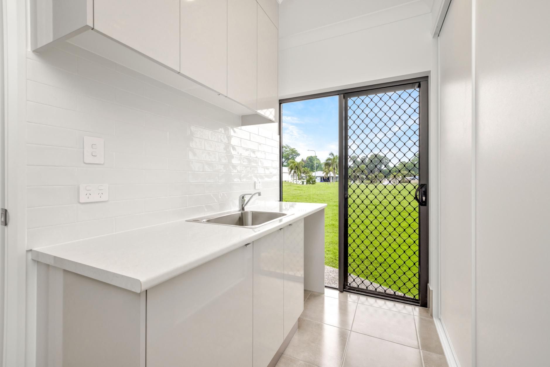 A Kitchen With White Cabinets, a Sink, and a Sliding Glass Door — Ashlee Jones Homes in Gordonvale, QLD