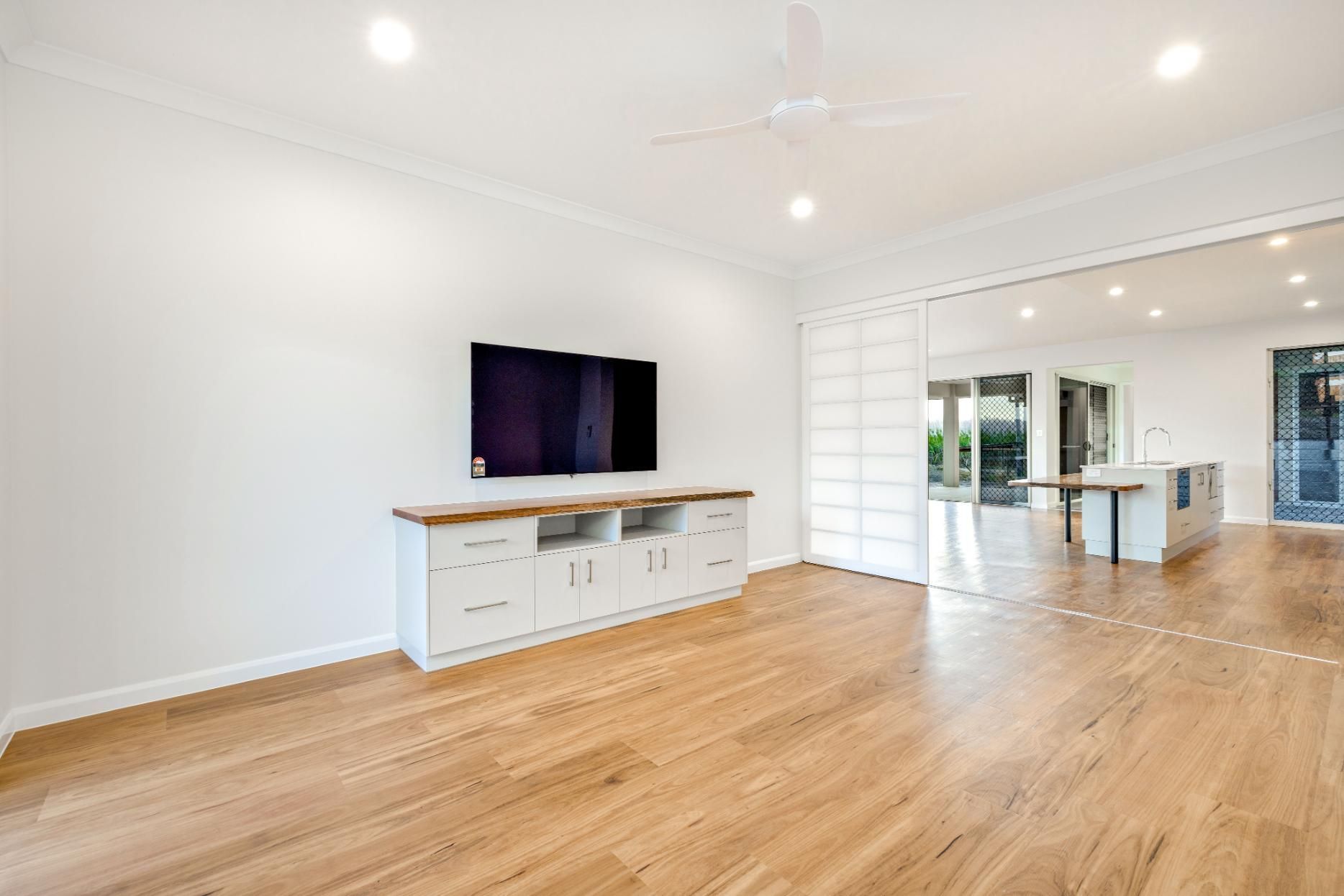 An Empty Living Room With Hardwood Floors and a Flat Screen Tv — Ashlee Jones Homes in Gordonvale, QLD