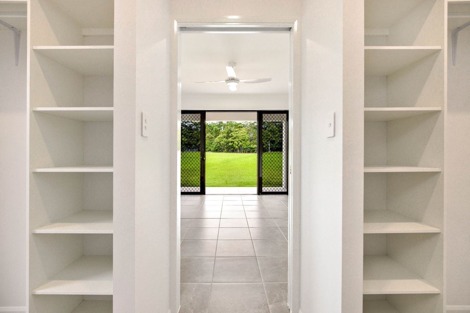 A Walk in Closet With Lots of Shelves and a Sliding Glass Door Leading to an Empty Room — Ashlee Jones Homes in Gordonvale, QLD