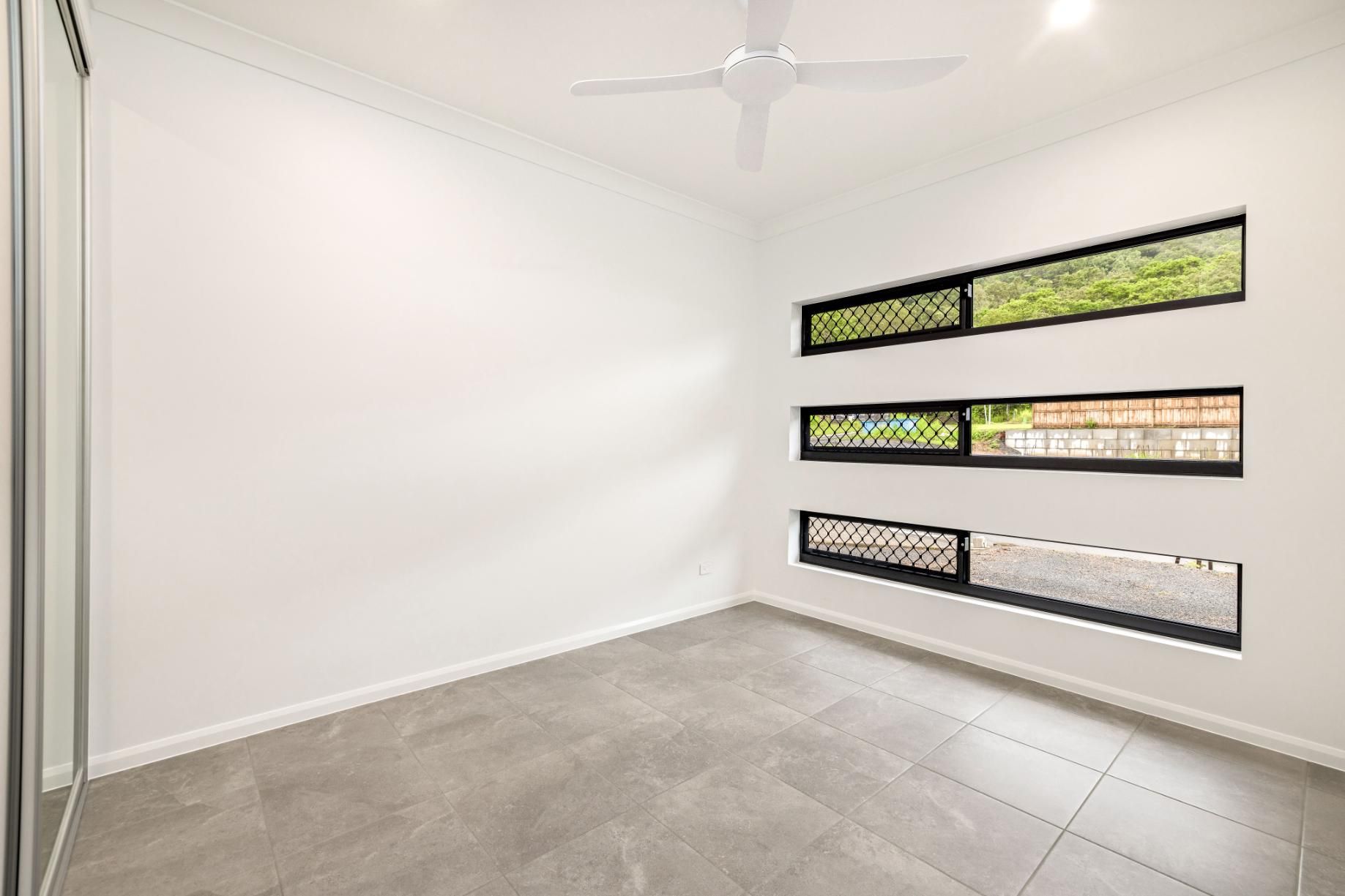 An Empty Room With Three Windows and a Ceiling Fan — Ashlee Jones Homes in Gordonvale, QLD