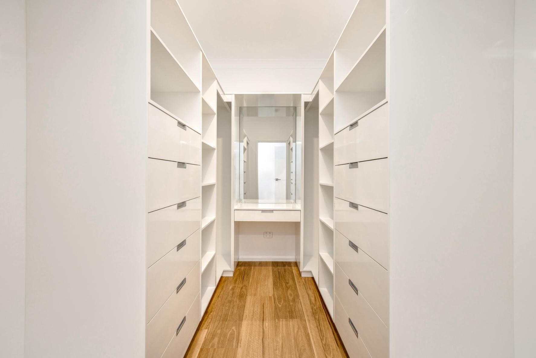 A Walk in Closet With White Shelves and Drawers and Wooden Floors — Ashlee Jones Homes in Gordonvale, QLD